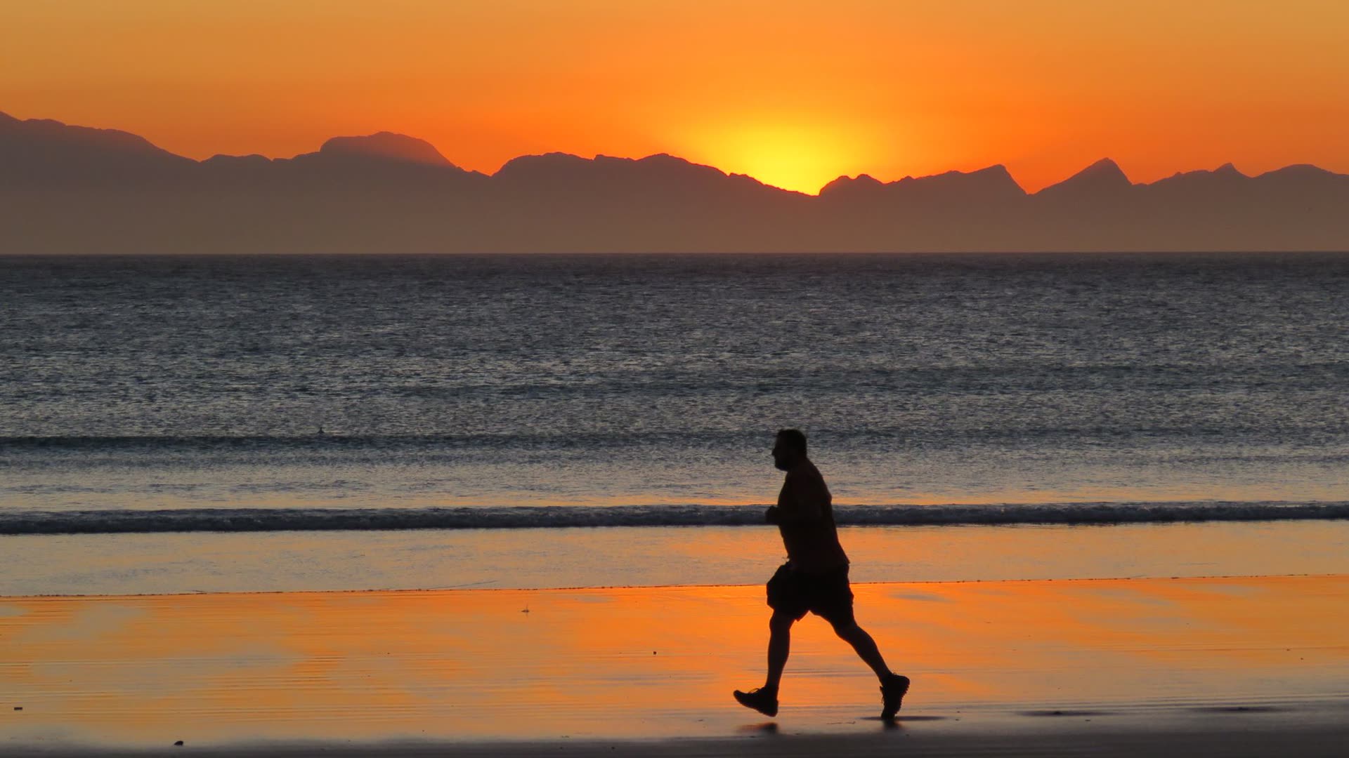 Runner on a beach at sunset with mountains behind