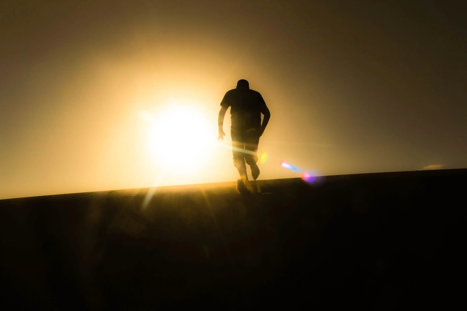 Silhouette of a runner climbing a hill into the sunrise