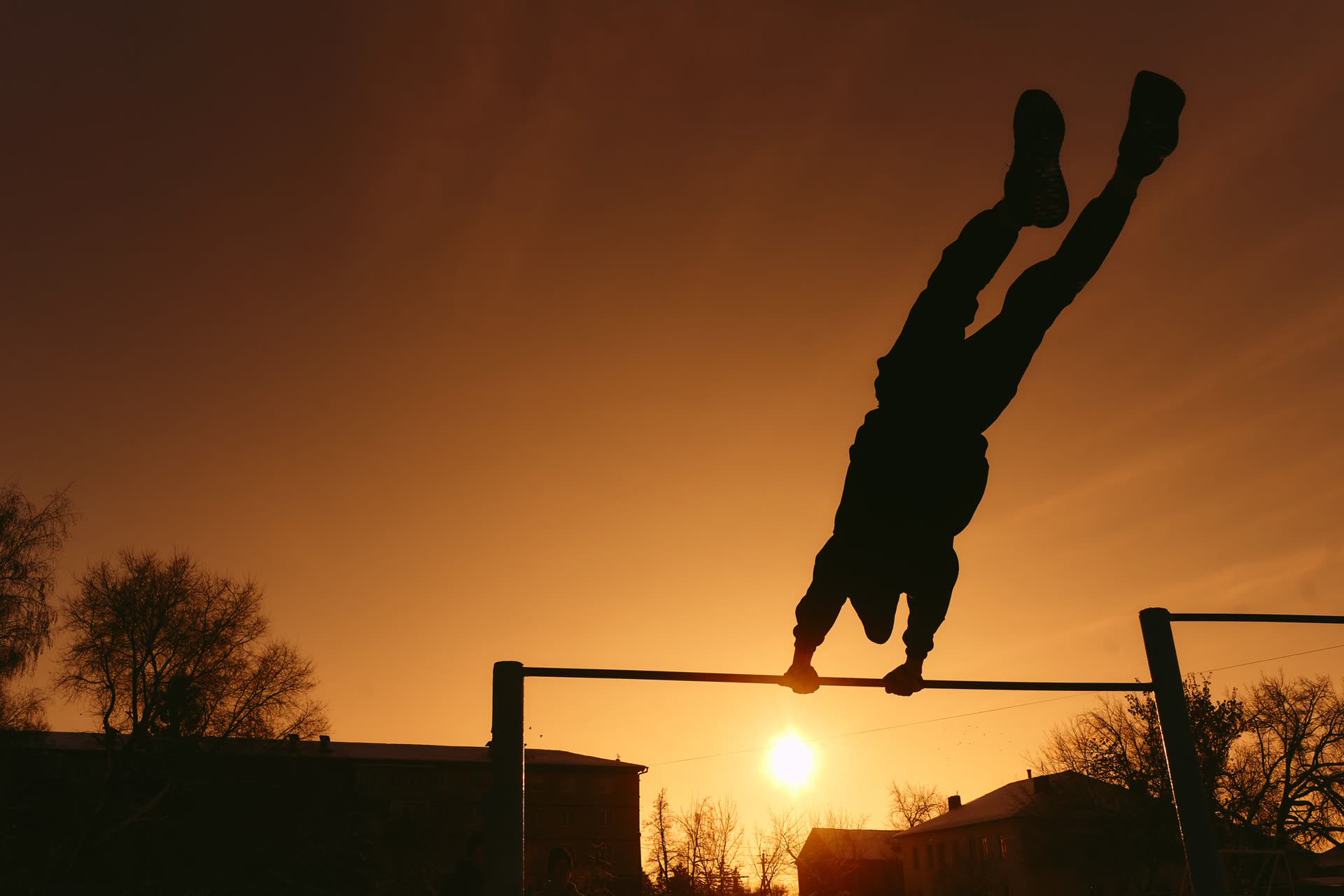 Silhouette of an athlete on a pull-up bar against a sunset sky