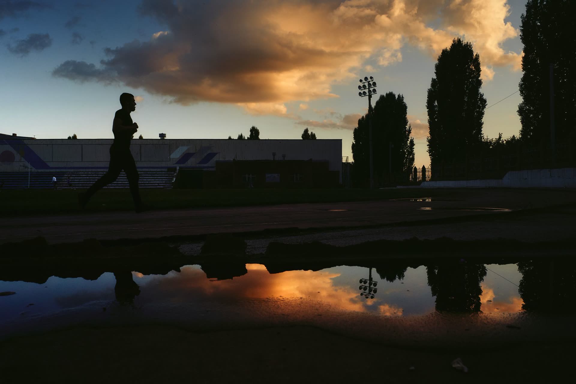 Silhouette of a runner on a track with a dramatic sky reflected in puddles